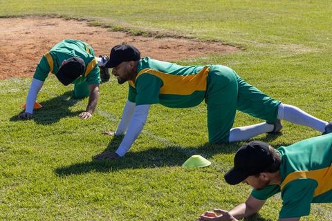 Baseball team crawling and stretching during outdoor warmup drills on grass infield
