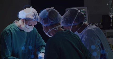 Surgical team performing operation in sterile hospital operating room with vital monitors