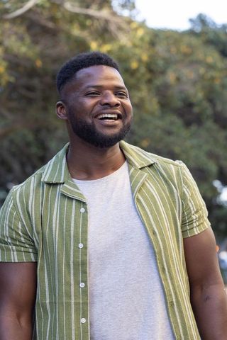 African american man smiling, looking upward in striped shirt during golden hour in park