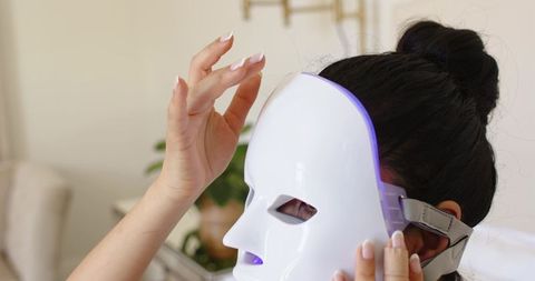 Woman applying led facial mask at home for skin rejuvenation, beauty routine, self-care