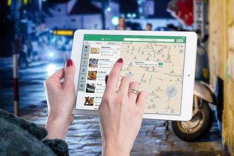 Woman navigating restaurant map on tablet tapping location while walking rainy city street