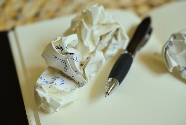 The scene depicts crumpled papers and a pen on an open notebook, indicating the challenges and frustrations of the creative process and brainstorming. This can be used for blog posts about writing difficulties, articles on overcoming writer's block, or promotional images for creative writing courses and workshops.
