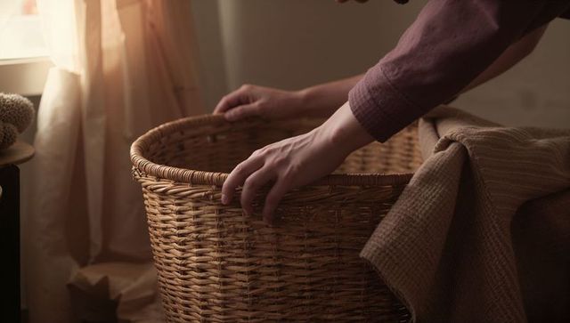 Adjusting wicker basket by sunlit window with cozy blanket and natural warm textures