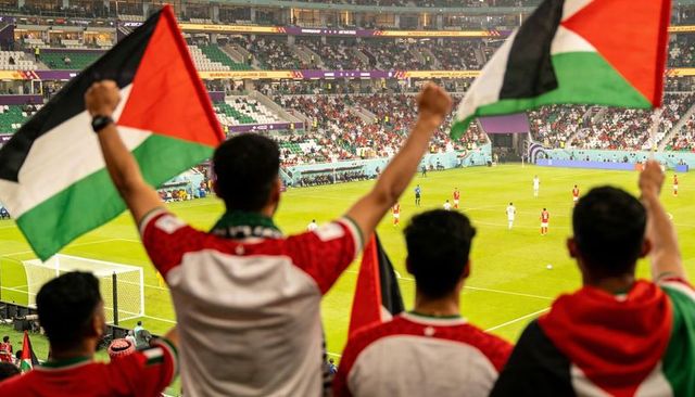 Waving palestinian flags cheering football fans wearing red and white in stadium