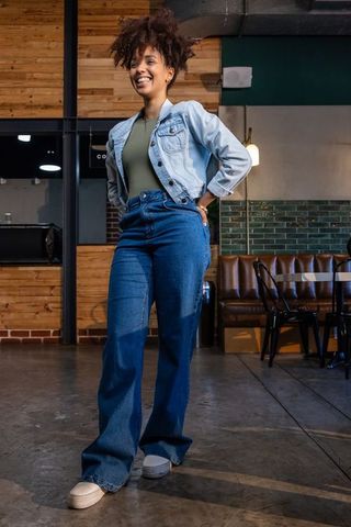 Confident african american woman smiling and standing in trendy cafe wearing denim jacket