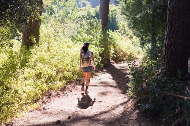 Rear view of young woman hiking on trail amidst plants in forest