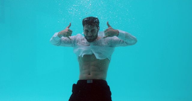 Man in formal attire underwater giving thumbs up, showcasing confidence and positivity. Can be used for business motivations, unique marketing concepts, adventurous campaigns, or playful and innovative advertisements.