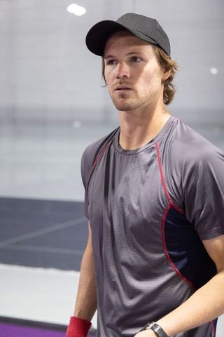 Focused male athlete standing on indoor court wearing black cap grey performance shirt and red wrist