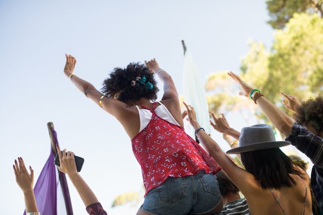 Tilt image of friends with arms raised against sky enjoying at music festival
