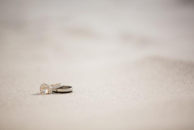 Visualizing close-up of wedding rings placed on sandy beach. Perfect for content related to beach weddings, engagement announcements, romantic getaways, or jewelry advertisements. Conveys a sense of romance, commitment, and scenic beauty, ideal for wedding blogs, event planning, and romantic vacation promotions.