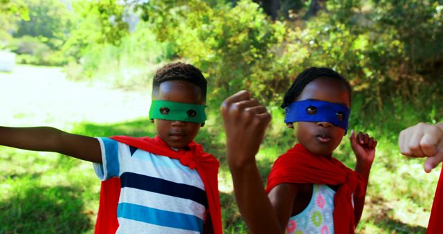 Children dressed in colorful capes and masks engage in imaginative superhero play in a lush green outdoor area. Perfect for concepts related to child development, creativity, imagination, playtime, and outdoor activities for kids. Useful for educational materials, family-oriented content, and promotional materials for children’s products.