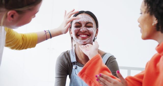 Women enjoying applying face masks together, having fun and smiling. Ideal for promoting skincare products, friendship, beauty routines, and self-care moments at home.
