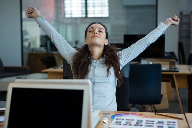 Graphic designer stretching her arms out in office