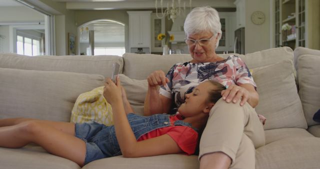 Happy caucasian grandmother with her granddaughter using tablet at home. Domestic life, family, technology and lifestyle, unaltered.