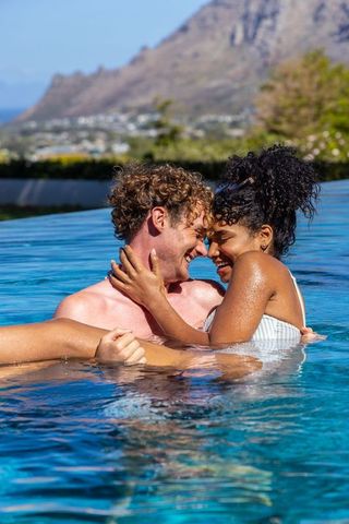 Couple embracing and laughing in infinity pool with ocean view and mountain backdrop