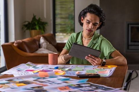 Asian man studying at home desk with tablet and colorful sticky notes planning creative project