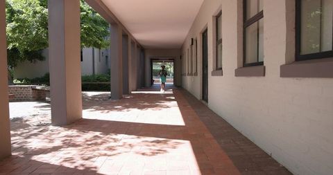 African American teen walking through sunlit campus colonnade with backpack and sun hat