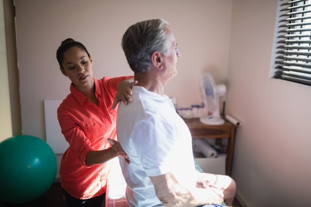 Young female therapist massaging back of senior male patient in hospital ward. Ideal for use in healthcare, wellness, and medical treatment contexts. Suitable for illustrating physical therapy, patient care, and rehabilitation services.
