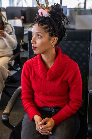 Young woman celebrating office holiday party wearing reindeer headband and red sweater