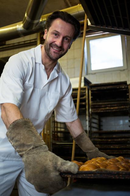 Smiling baker keeping tray of baked buns in shelf