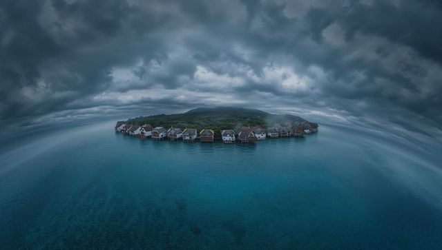 Storm clouds gathering over curved stilt houses on tropical reef island, aerial seascape