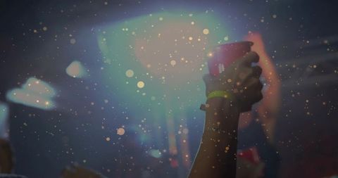 Female arm raising red cup at concert with neon wristband, confetti bokeh lights