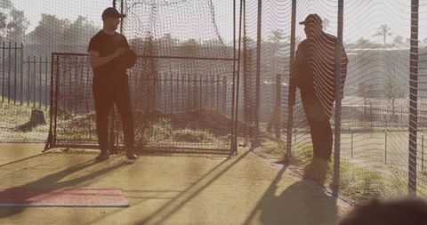 Sunlit senior baseball coaches mentoring in outdoor batting cage casting dramatic shadows