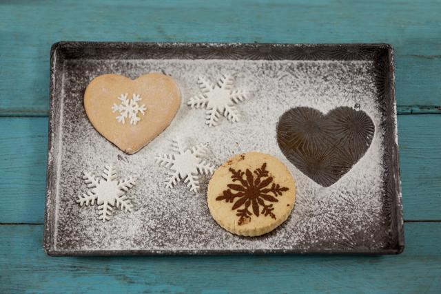 Gingerbread cookies with intricate snowflake designs and heart shapes dusted with icing sugar on a rustic tray. Ideal for holiday-themed promotions, Christmas baking blogs, festive recipe books, and winter dessert advertisements.