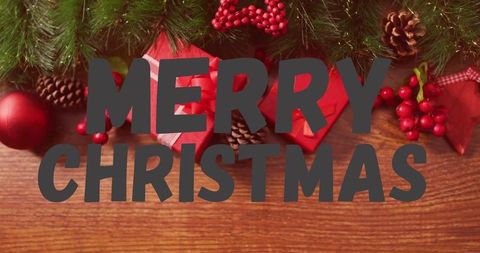 Merry christmas lettering on rustic wood tabletop with pine garland and red gifts