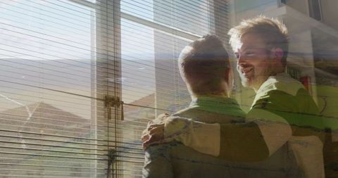 Two men embracing by sunlit window with venetian blinds, cozy home intimacy