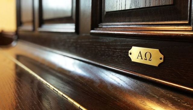 Brass alpha omega nameplate on dark oak church pew paneling with polished wood grain