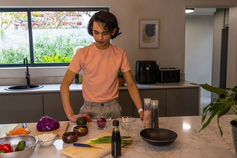 Young asian man preparing avocado and rice on marble kitchen island in modern bright home