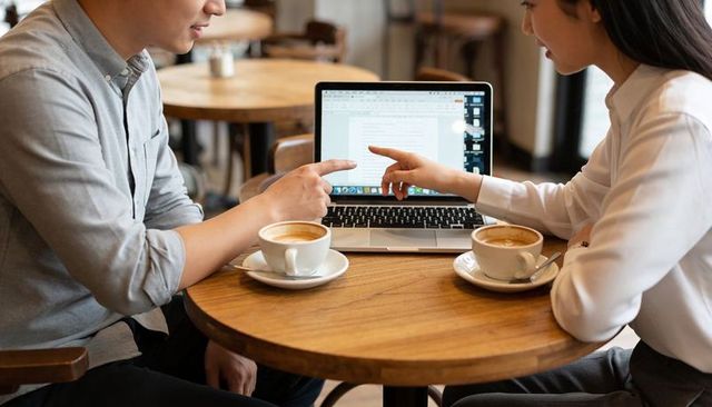 Asian colleagues pointing at laptop while collaborating over coffee in casual cafe