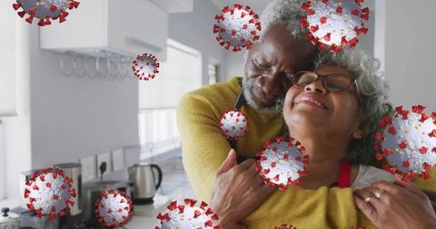 Elderly couple embracing amidst virus symbols in home kitchen