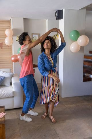 Friends dancing and celebrating at home with pastel balloons and banner