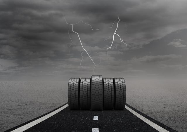 This image depicts a set of tyres on a road under a stormy sky with lightning. The dark clouds and overcast weather create a dramatic and intense atmosphere. This image can be used for automotive advertisements, weather-related articles, safety campaigns, and transportation-themed content.