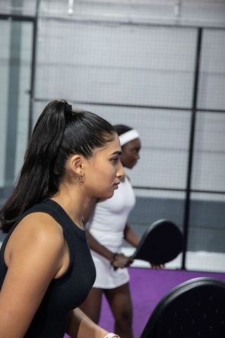 Diverse women training padel on purple indoor court with focused teamwork