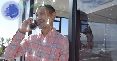 Smiling man talking on smartphone at balcony window with coastal ocean view and reflection