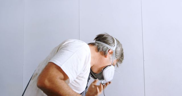 This image shows a worker in a white protective respirator inspecting large equipment. Ideal for health and safety communications, industrial safety procedures, and protective gear promotions. Can be used in articles, blogs, or websites focusing on workplace safety and industrial maintenance. Perfect for illustrating safety practices in industrial environments.