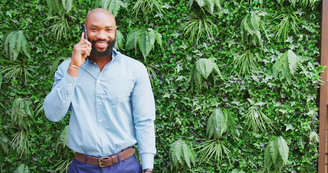 Smiling Man on Phone Against Lush Green Wall - Download Free Stock Images Pikwizard.com