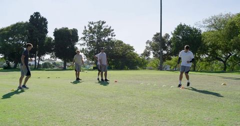Diverse male teammates sprinting through cone drill on park field for agility training