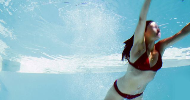 Woman swimming underwater in a pool wearing red bikini. Great for summer theme, fitness and exercise promotions, swimwear ads, pool-party invitations, and relaxation concepts.
