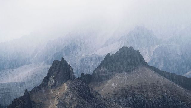 Jagged alpine peaks shrouding in mist and rain creating moody rugged mountain panorama