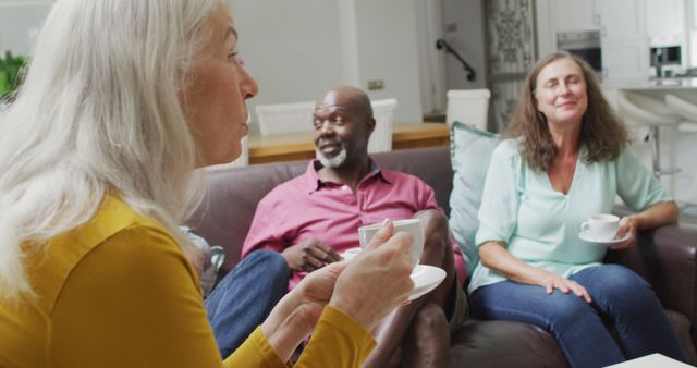 Senior friends sitting together on a couch, drinking coffee, and chatting in a cozy living room. Perfect for depicting social interaction, retirement lifestyle, senior community, or homey atmosphere in marketing materials, websites, and publications.