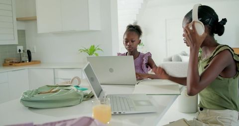 School-age girls studying and working at modern kitchen island with laptops and headphones