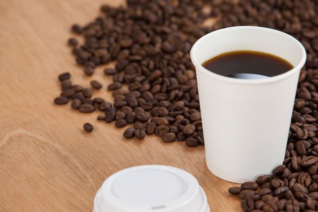 Coffee beans and black coffee in disposable cup on wooden background