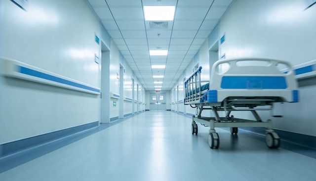 Empty hospital corridor featuring wheeled gurney, sterile lighting, clinical handrails