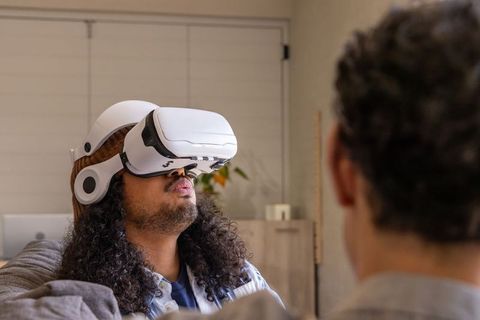 African American man experiencing virtual reality headset while friend watches on cozy sofa
