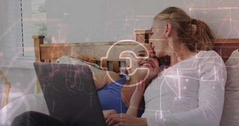 Lesbian couple kissing and cuddling on bed while using laptop, romantic cozy morning at home