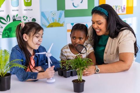Diverse teacher guiding children in sustainability examining plants and wind turbine